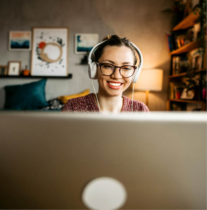 Young woman teaching online from her living room. Young woman wearing headphones while having a video call and looking at the camera.